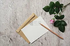 原型空白白色贺卡或邀请，牛皮纸棕色信封，铅笔和粉红色玫瑰花在灰色的背景。平躺，俯视图。副本的空间。