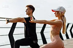 年轻的健身夫妇在海上的桥上做伸展运动，好动的男人和女人一起锻炼