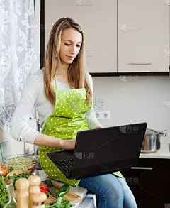 普通女孩穿着围裙用笔记本做饭