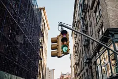 Urban City StreetA low angle view of towering buildings standing tall in new york city on a sunny day with a clear sky, traffic lights can be seen in the foreground of the image.