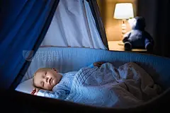 Baby boy sleeping in blue crib at night