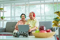 一对老年夫妇正在家里沙发上的笔记本电脑上用视频通话技术向家人挥手