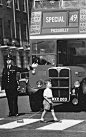 A boy crosses in front of a double-decker bus, pulling a miniature version behind him.  1950s, UK.: 