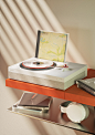 Vivia turntable for compact discs set on an orange floating shelf with a Brian Eno compact disc on display and on the player's platter. Underneath on a second level shelf are more CDs and a pair of white headphones.