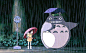 This may contain: a person holding an umbrella standing in the rain with a totoro behind them