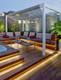 Diseño de terraza con un cómodo sofá,  suelo de madera y luz indirecta: 