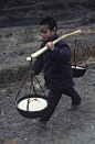 1989，柳州，三江，独峒乡，八协村，一个孩子正前去参加一场婚礼，用扁担挑着满满的两盆大米作为礼物。他收到了一支别人送的香烟—夹在他耳朵后面