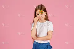一个惊讶的小女孩的肖像拿着心形棒棒糖，看着孤立的相机在粉红色的背景