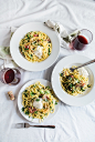 An overhead shot of two glasses of red wine next to three plates of pasta with pancetta on a white tablecloth