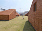 These angular chimney-like structures burst through the roof of the building, creating wooden sheds that are used as seating areas and hiding places for children playing on the rooftop lawn.