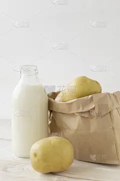 白木背景，装在玻璃瓶里的土豆牛奶。桌上的牛皮纸袋子里装着新鲜的土豆