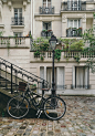 A bicycle resting against a flight of stairs and a lamppost with French buildings in the background.