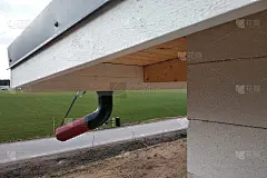 正在施工的建筑物外立面有未完工的墙壁和木制屋面板和塑料排水沟管。