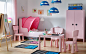 Kid’s bedroom with white walls and a light pink bed, wardrobe and tables and chairs.