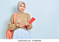 Smiling young Asian Muslim woman student in brown sweater with backpack, holding book and mobile phone isolated on white background. back to school concept 库存照片
