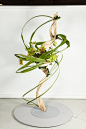 This may contain: a sculpture made out of branches and flowers on a white pedestal in front of a wall