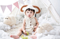 baby sitting beside white sheep plush toy