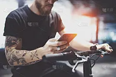 一名戴着墨镜的纹身男子骑着电动车在城市里发短信。