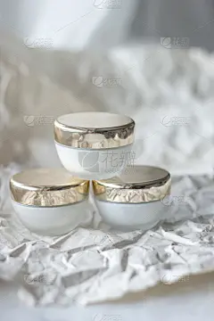 三个白色玻璃护肤罐，金色盖子，象牙背景