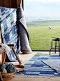 Barn-like display room with wool TRANGET flatwoven rugs in shades of blue rectangles, shown on a floor and draped on a wall.