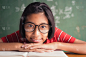 一个戴眼镜的亚洲女孩正在课堂上的黑板上微笑着看书