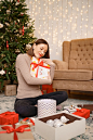 Woman embracing a gift box while sitting between many presents in the christmas decorated living