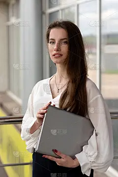 一个美丽的年轻女子的肖像，浅黑色长发，穿着白色衬衫，在城市的户外笔记本电脑。