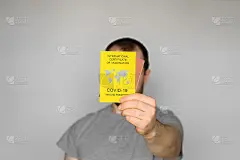 成人男子身穿t恤，手持黄色国际疫苗接种证书，背景为灰色。旅行免疫护照，证明接种了Covid-19疫苗
