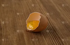 中间打碎一个带蛋黄和蛋白质的生鸡蛋，放在一张棕色的木桌上，侧视图。