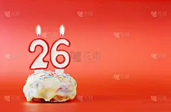 二十六岁生日。纸杯蛋糕，上面有燃烧着的白色蜡烛，形状是26号。鲜艳的红色背景与复制空间