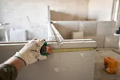 建筑工人用卷尺测量石膏板。公寓的内墙使用带槽脊的石膏混凝土板。企口石膏块