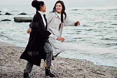 两个漂亮时髦的女孩穿着风衣在海边快乐地奔跑