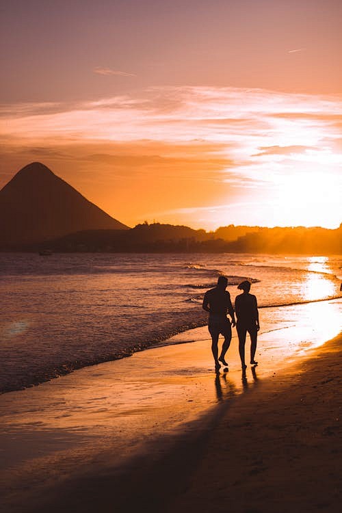 免費 兩人在日落時在海灘上行走的剪影 圖...
