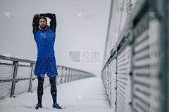 在一个冬天的雪天，一名男子在桥上训练前做伸展运动。