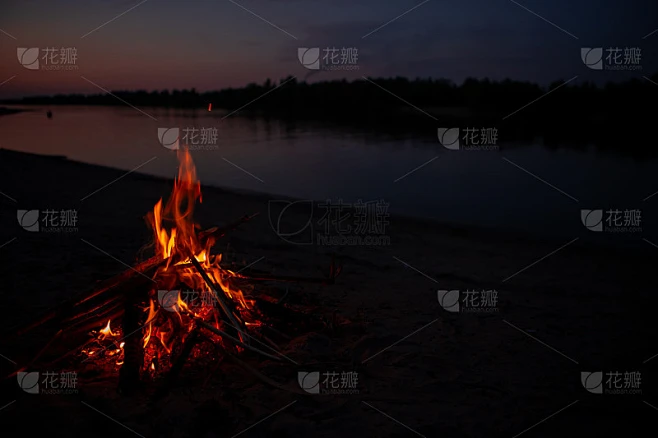晚上河边放篝火。夏天，水库附近燃烧的树枝和柴火发出红色的火焰。在火旁的户外消遣。素材-花瓣网