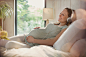 Smiling pregnant woman relaxing listening to music with headphones in bed by Caia Images on 500px
