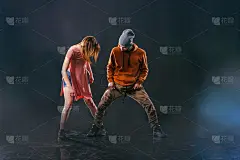 一对情侣在跳现代舞，展示他们的腿部伸展动作。黑色的背景，而这对夫妇穿着城市色彩鲜艳的衣服。