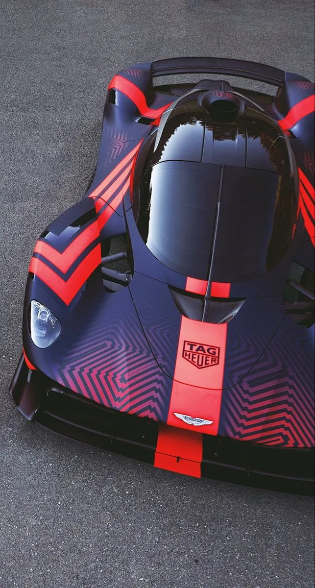 This may contain: a blue and red race car on the road with its hood up ...