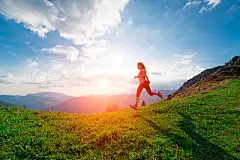 Female athlete trains running in the hillside meadows at sunset