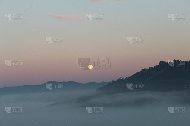 早晨的月亮在红色的天空和雾的山丘上