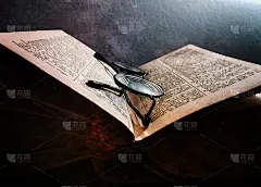 一本翻开的很旧的书，上面有旧眼镜。这本书的年代是由书页的颜色来确定的，书页很黄。这款眼镜的镜框是经典