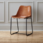 roadhouse leather chair : saddle up.  Handmade leather composite with natural hide tones and markings saddles a contoured seat edged with a handsewn whipstitch and brass-painted rivets.  Rides modern on hand-welded matte black iron frame that flows contin
