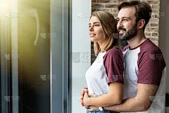 一个年轻人拥抱着他的女朋友，两人都从窗户往外看