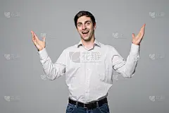 年轻惊讶的男子肖像，一个自信的商人显示双手在灰色的背景。