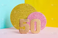 金色数字“50”在多色蓝黄粉背景和两个闪亮的金色和粉红色圆圈。生日贺卡的概念。