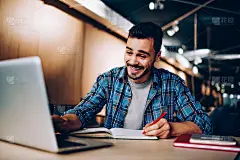 快乐的嬉皮士在图书馆准备家庭作业的时候嘲笑着在笔记本电脑上浏览社交网络的内容，快乐的男学生一边学习一