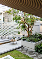 This may contain: an outdoor living area with couches, tables and plants on the grass in front of a white fence