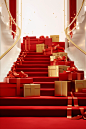 Red ribbon leading down stairs with red boxes, in the style of gold leaf accents, minimalist sets, piles/stacks, festive atmosphere, ready-made, wrapped, 32k uhd