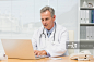 Focused doctor sitting at his desk using his laptop in his office at the hospital_创意图片