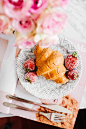 croissant bread and stawberries on beside fork and knife